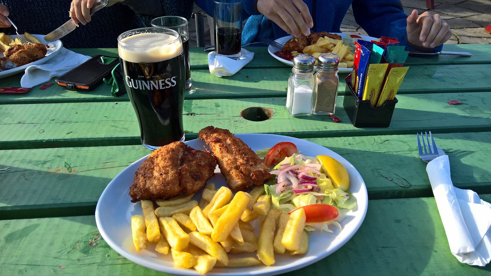 Fish and chips with salad and a pint of Guinness on an outdoor table