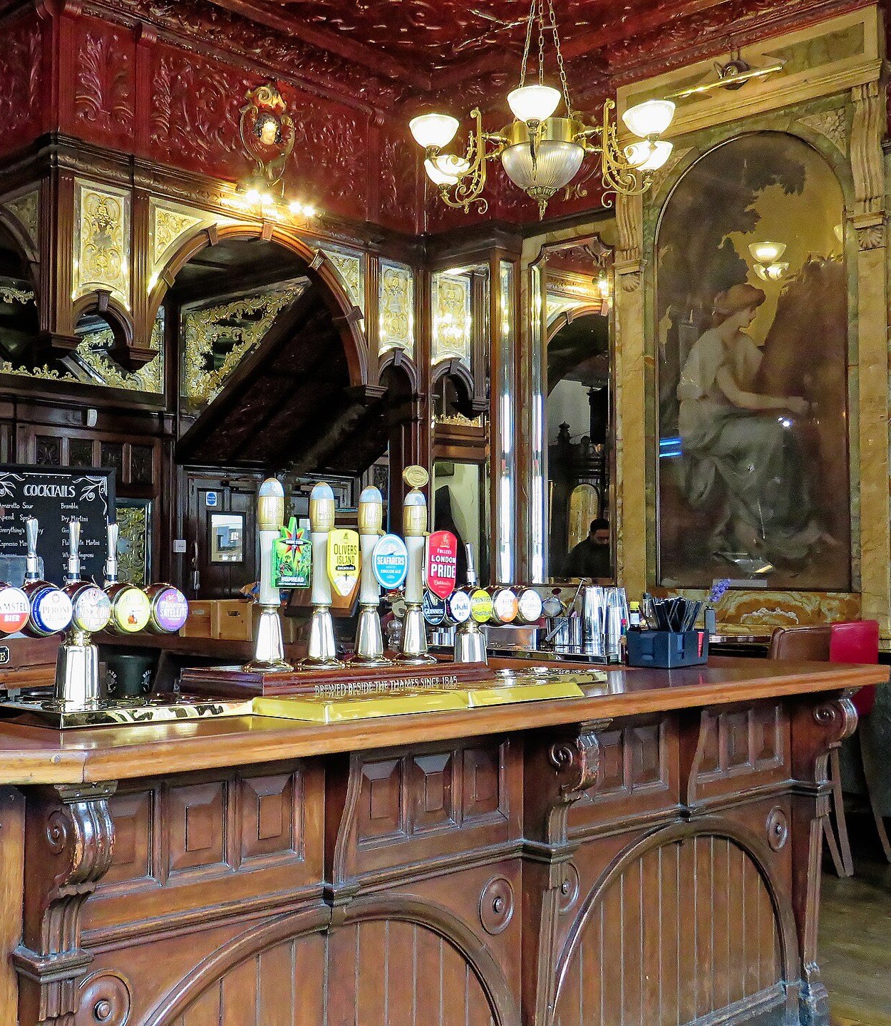 A heritage pub bar counter in dark carved timber with brass hand pumps and mirrors