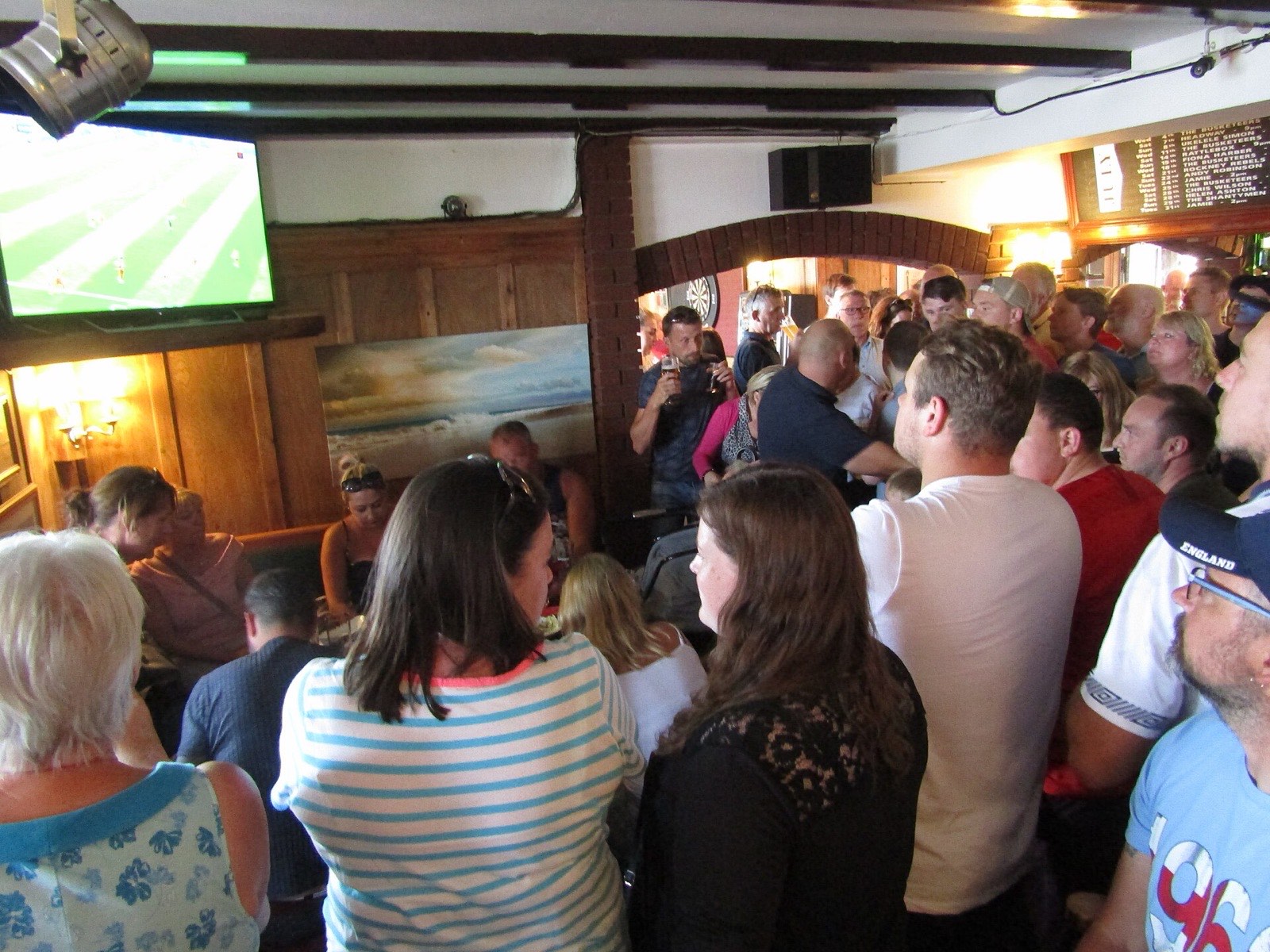 A packed pub crowd watching a football match on the big screen